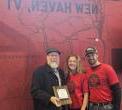 Fred, Tamara & Joey stand in front of a red wall painted with a Vermont map